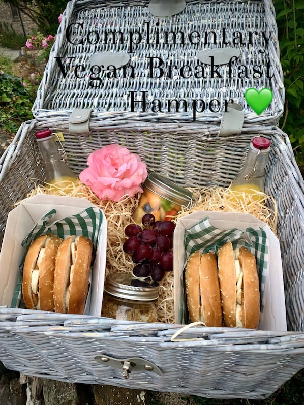 A wicker basket with two containers of vegan breakfast sandwiches, a bottle of juice, and a pink flower. - Rame- 2 Bedroom Safari Cabin Tent (Torpoint)