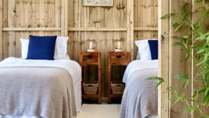 A room with two beds, wooden walls, a framed picture, and a small table with a lamp. - Rame- 2 Bedroom Safari Cabin Tent (Torpoint)