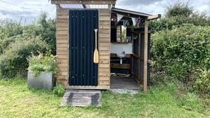 A small wooden structure with a black door, a wooden paddle, and a sink. - Rame- 2 Bedroom Safari Cabin Tent (Torpoint)