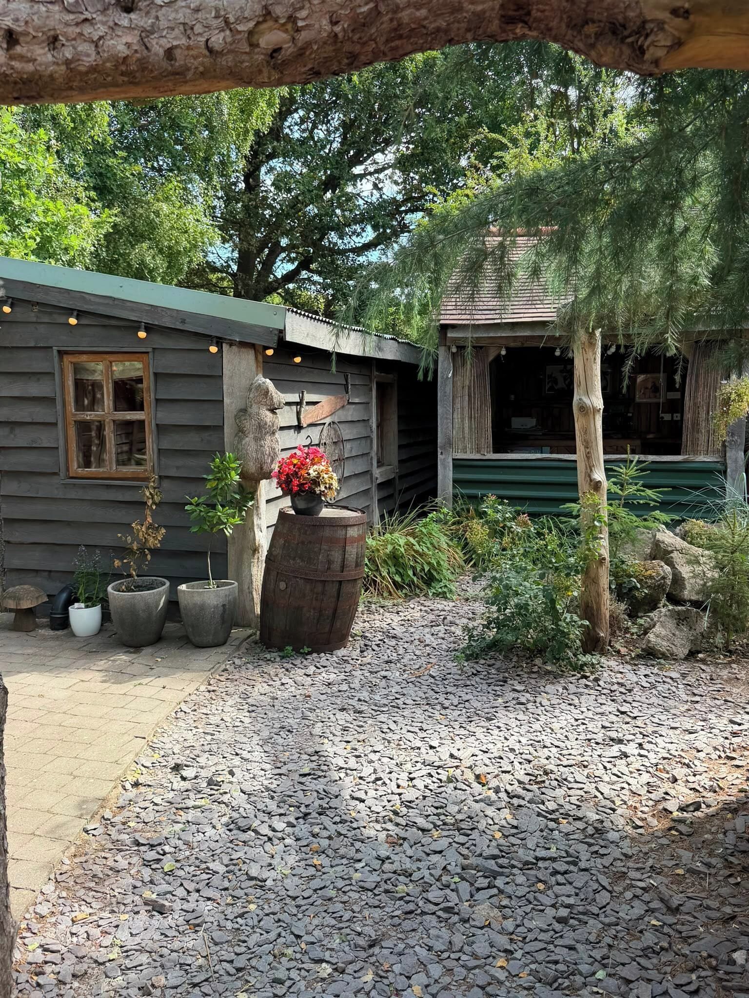 A rustic cabin with a wooden exterior, a stone statue, and a gravel driveway.