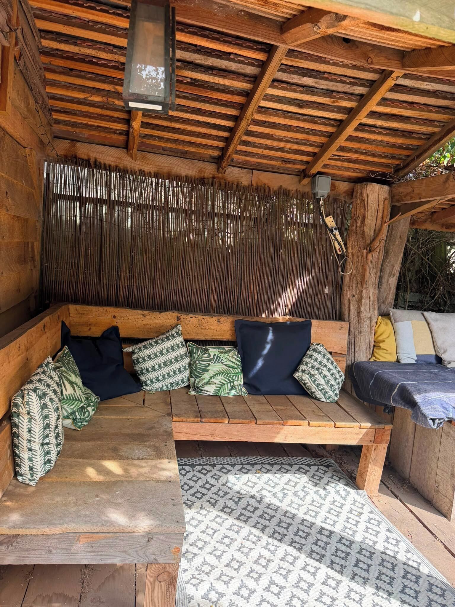 A wooden bench with cushions, a woven wall, and a hanging light fixture.