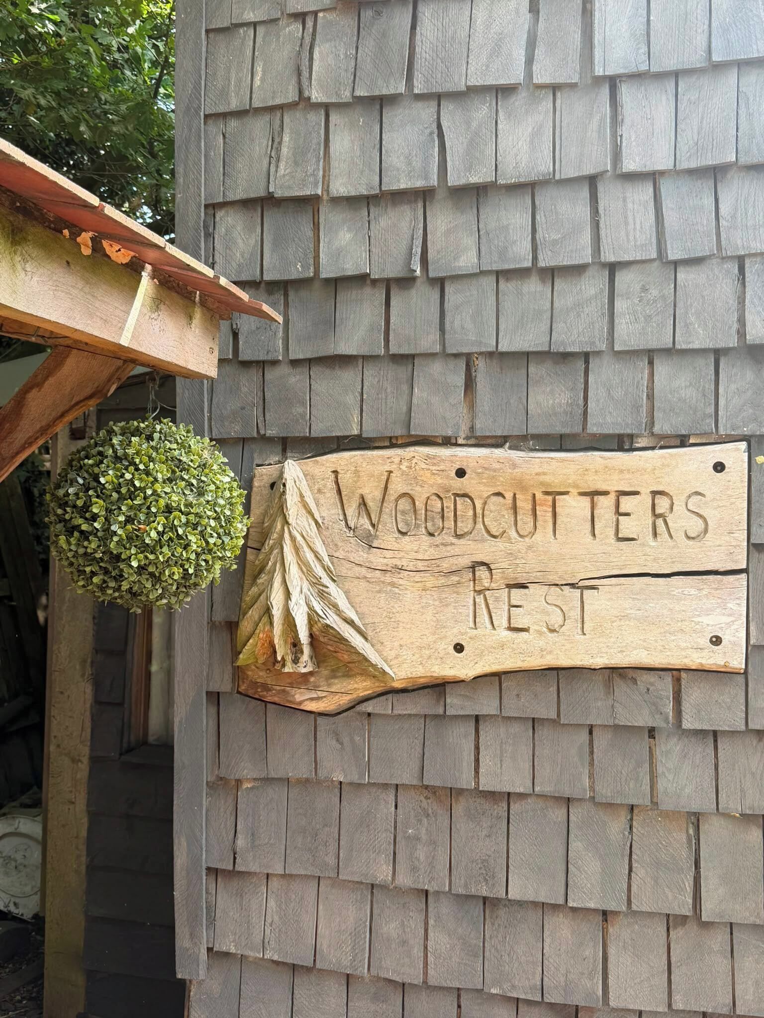 A wooden sign with the text 'WOODCUTTERS REST' mounted on a shingled wall.