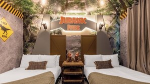 Une chambre à thème avec deux lits, une table de chevet en bois et une enseigne « Jurassic Park ».