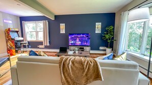 En stue med sofa, fjernsyn, spillekonsol og en plante.
