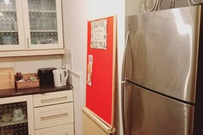 Une cuisine équipée d’un réfrigérateur en acier inoxydable, d’un tableau d’affichage rouge et d’un plan de travail sur lequel se trouvent un grille-pain et une bouilloire.