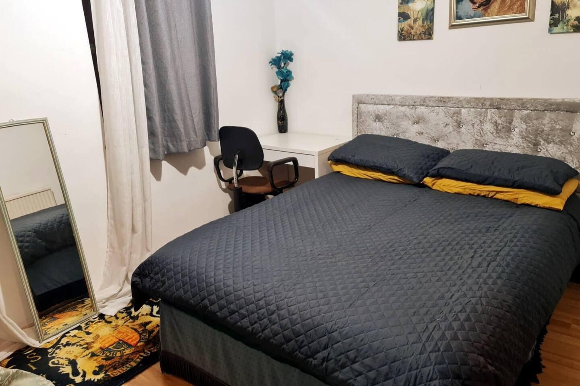 A bedroom with a bed, a desk, a chair, and a mirror.