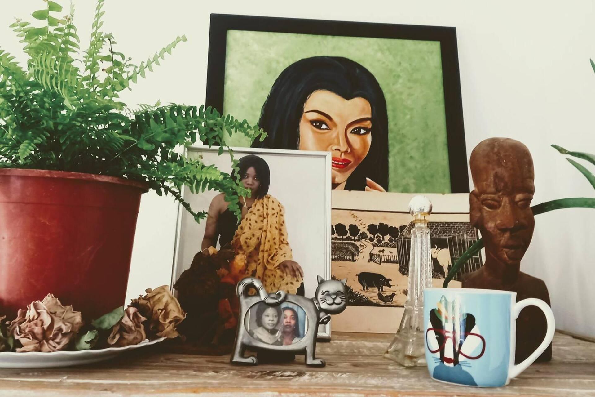 Uma prateleira com uma planta em vaso, um retrato emoldurado, uma caneca e uma pequena estatueta.
