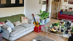 A living room with a grey sofa, a red armchair, a glass coffee table with fruits and drinks, and a guitar. - Lovely 2-bed Apartment in Battersea, London (London)