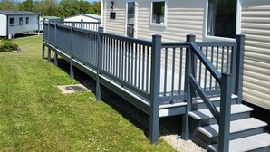 A row of mobile homes with a wooden deck and steps leading to the entrance. - Static Caravan - The Dizzard (Holsworthy)