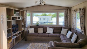 A cozy living room with a brown sofa, a wooden bookshelf, and a television. - Static Caravan - The Dizzard (Holsworthy)