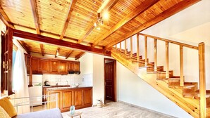 A spacious room with a large bed, a wooden staircase, and a kitchen area.