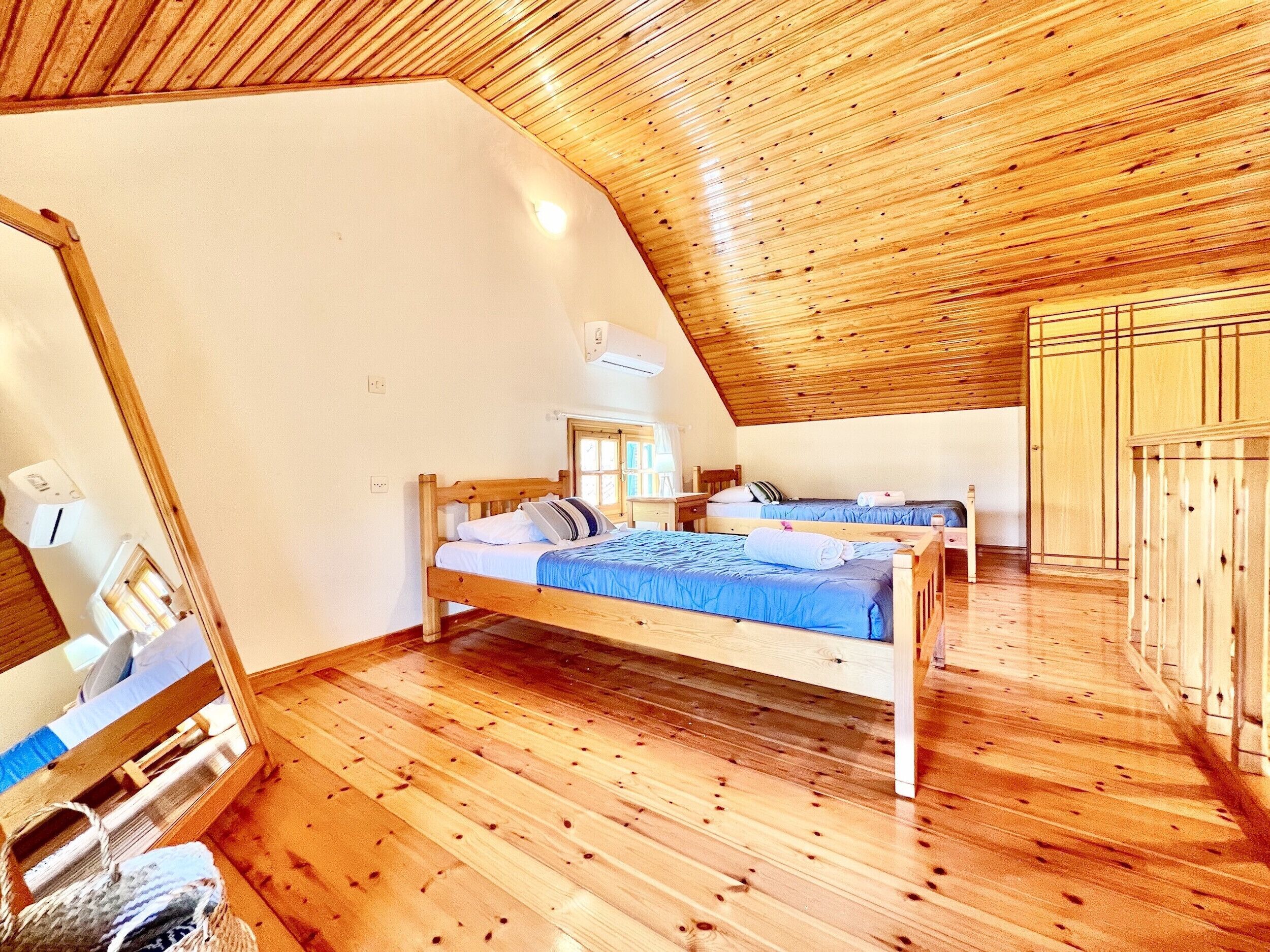 A room with a sloped ceiling, wooden flooring, a bed with blue bedding, and a window with blinds.