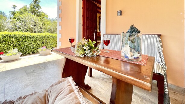 A wooden table set with a vase of flowers, two wine glasses, and a decorative glass container.