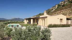 A single-story building with a swimming pool, surrounded by greenery and a mountainous backdrop.