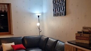 A living room with a black leather sofa, a round coffee table, a wooden cabinet, and a wall-mounted light fixture.