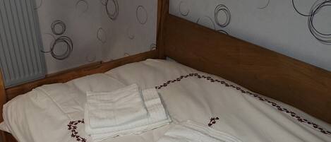 Una cama bien tendida con sábanas blancas y bordados florales decorativos, un cabecero de madera y una pared con un diseño circular.