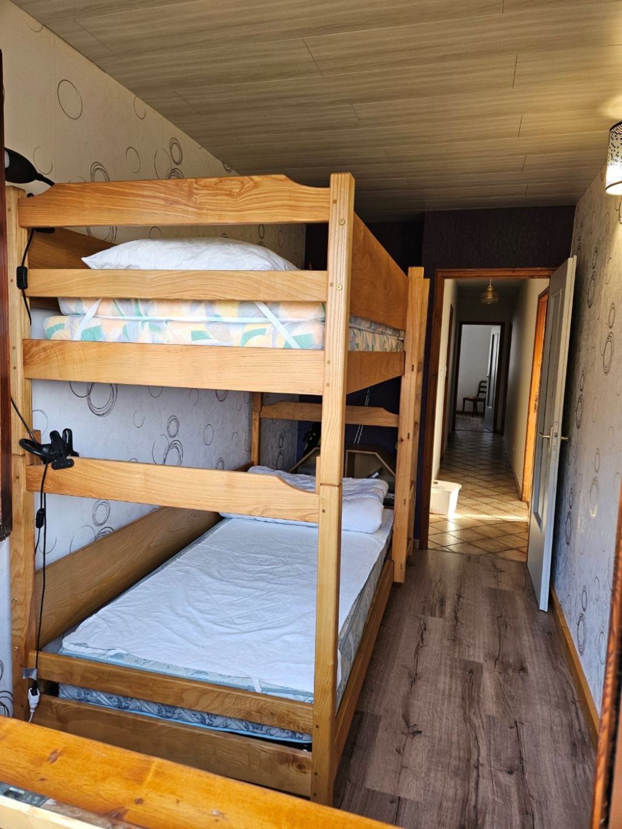A bunk bed room with wooden frames, a mattress, and a pillow.