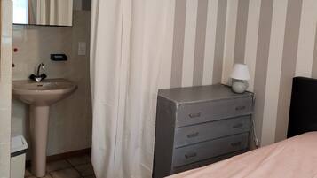 Un dormitorio con cama, mesita de noche con lámpara, cómoda, lavabo y pared a rayas.