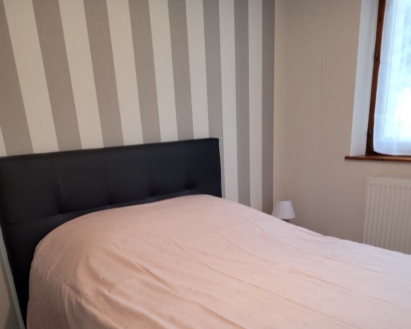 A bedroom with a bed, a nightstand, a lamp, and a window with curtains.