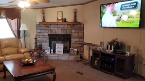 A living room with a stone fireplace, leather sofa, and a television displaying 'UNMATCHED ACCURACY'. - Home Away from Home (Natchez)