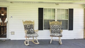 Two rocking chairs with ornate wooden frames and patterned upholstery, positioned outside a white house with black shutters. - Home Away from Home (Natchez)