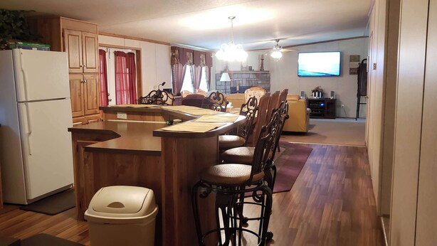 A kitchen with wooden cabinets, a refrigerator, a dining area with a table and chairs, a television, and a ceiling fan. - Home Away from Home (Natchez)