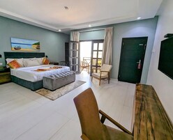 Habitación de hotel con cama, zona de estar, una mesa y vistas a través de una puerta.