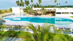 A swimming pool with lounge chairs and a covered seating area, surrounded by palm trees and a view of the ocean. - Breezes  Beach Resort (Ekumfi Narkwa)