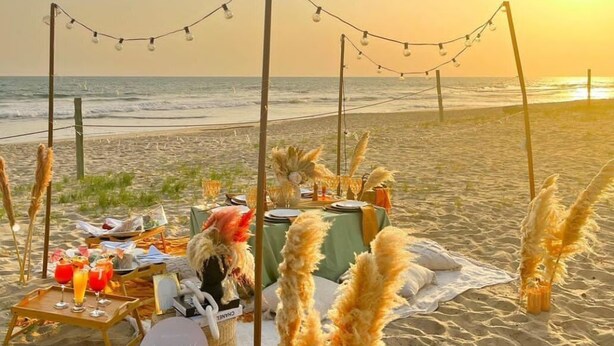 A beachside dining setup with a table, chairs, and a basket labeled "luxury picnic." - Breezes  Beach Resort (Ekumfi Narkwa)
