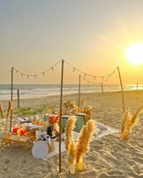 A beachside dining setup with a table, chairs, and a basket labeled "luxury picnic."