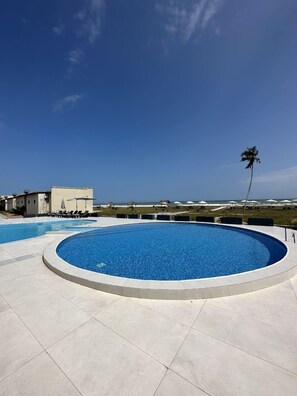 A circular swimming pool with a clear blue sky and a palm tree in the background.