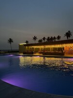 Piscina com área de bar e palmeiras ao fundo.