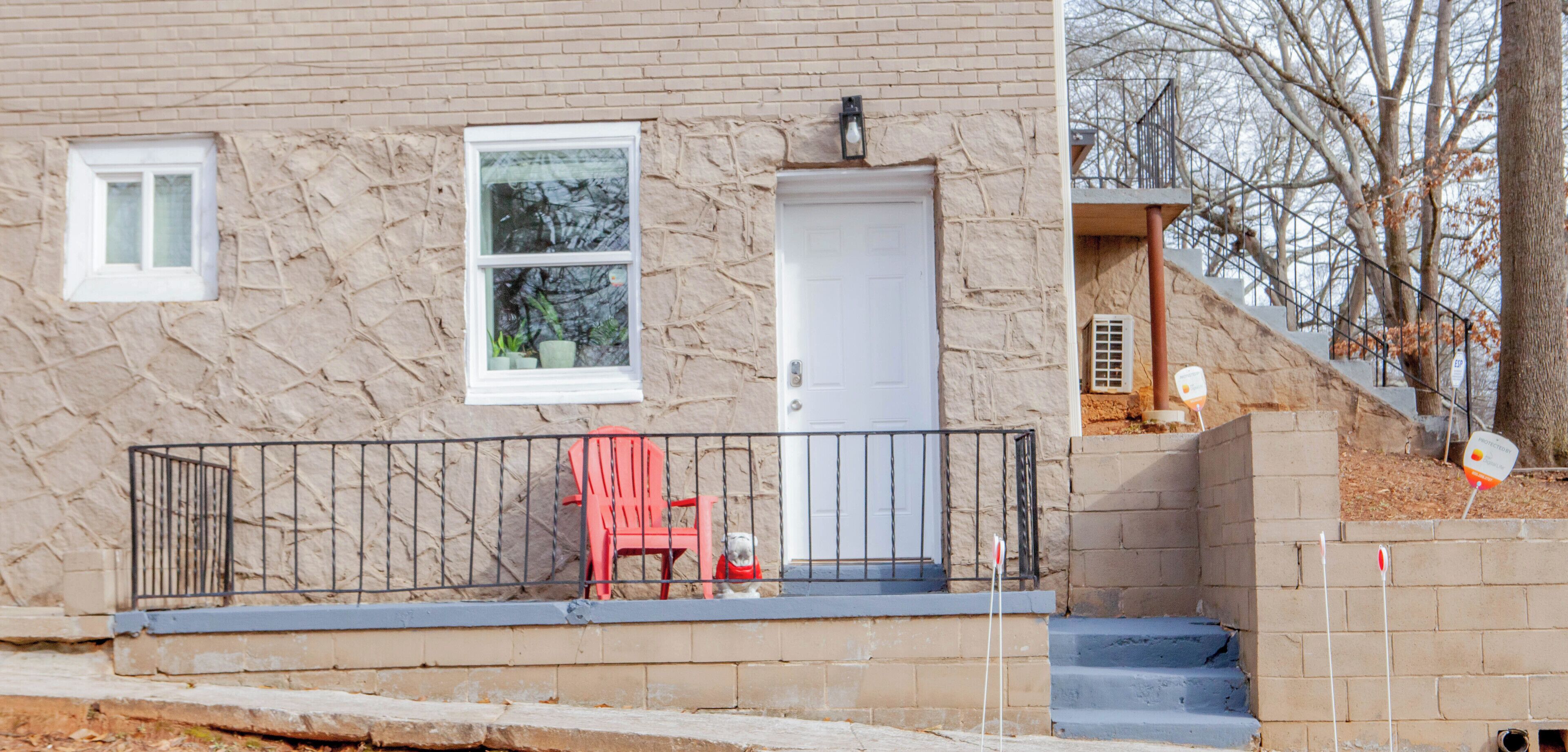 A house with a stone facade, a white door, a small balcony with a red chair, and a staircase leading to a covered porch area.