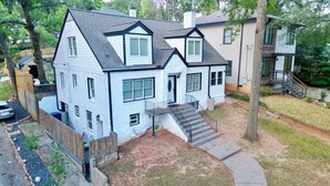 A two-story house with a front porch, a staircase leading to the entrance, and a small front yard. - Cozy Basement Suite with Full Kitchen, Walk to Edgewood (Atlanta)