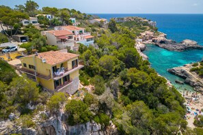 Une propriété située sur la côte, comprenant plusieurs bâtiments, une plage rocheuse et des eaux d’un bleu cristallin.