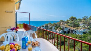 A balcony with a table set for breakfast, overlooking a coastal landscape.