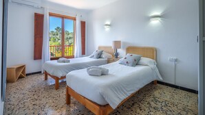 A room with two beds, a window with curtains, a wooden bench, and a wall-mounted lamp.