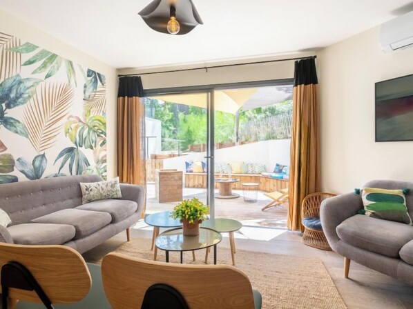 A living room with a grey sofa, a round coffee table with a plant, and a view of an outdoor patio area with a table and chairs.