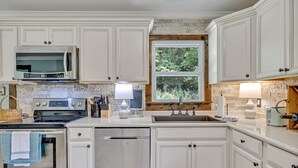 A kitchen with white cabinets, a microwave, stove, oven, and dishwasher. There is a window with a view of trees and a sink with a faucet. - Serene Hilltop Getaway - Near Lieper's Fork (Santa Fe)