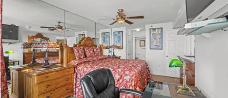 A bedroom with a bed, a desk, a chair, a dresser, a mirror, and a ceiling fan.