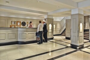 Welcome to our hotel lobby, featuring a central reception desk and staircase.