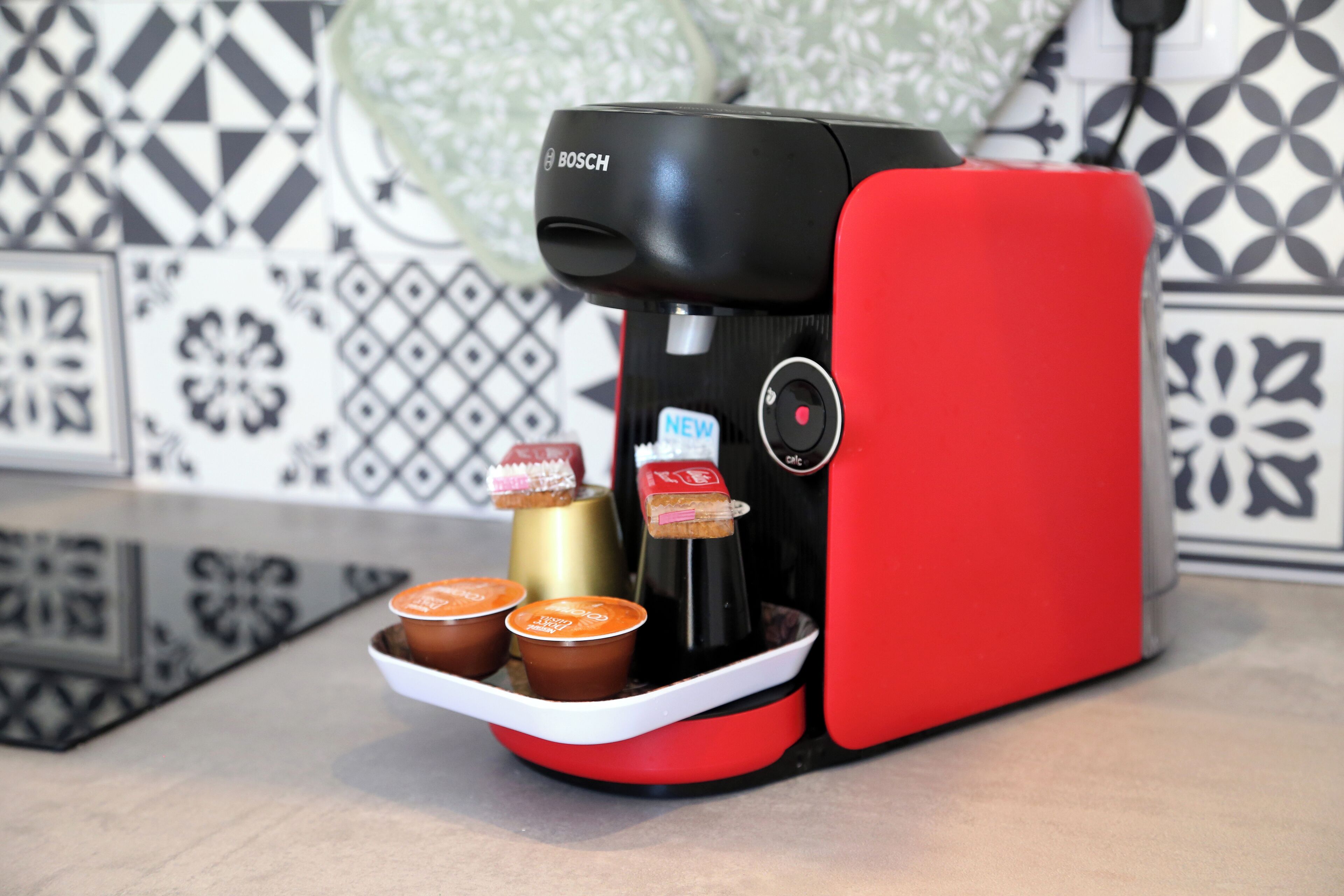 A red and black coffee maker with a tray holding three cups and a bottle.