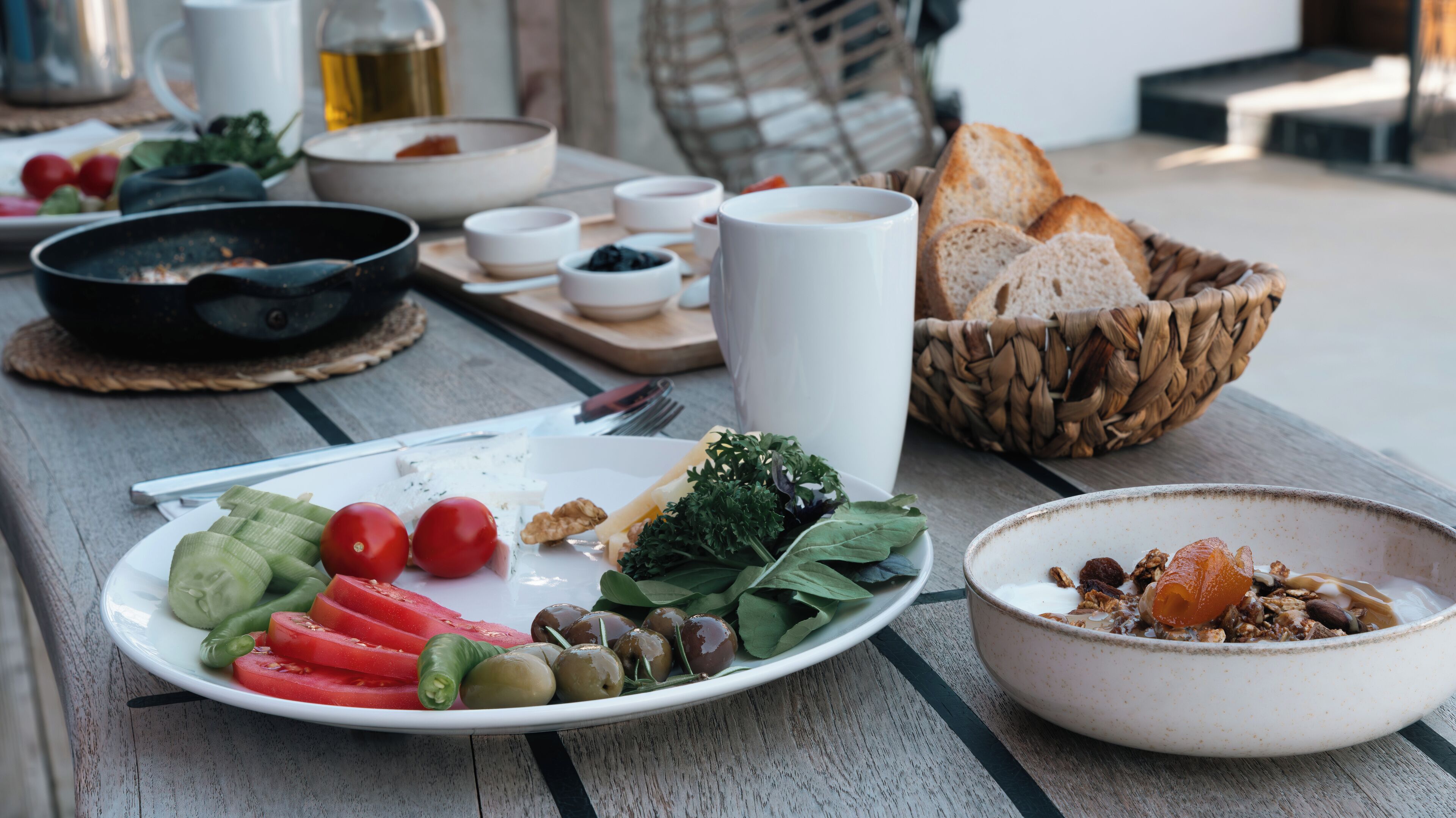A breakfast setting with a plate of fresh vegetables, a bowl of cereal, and a basket of bread.