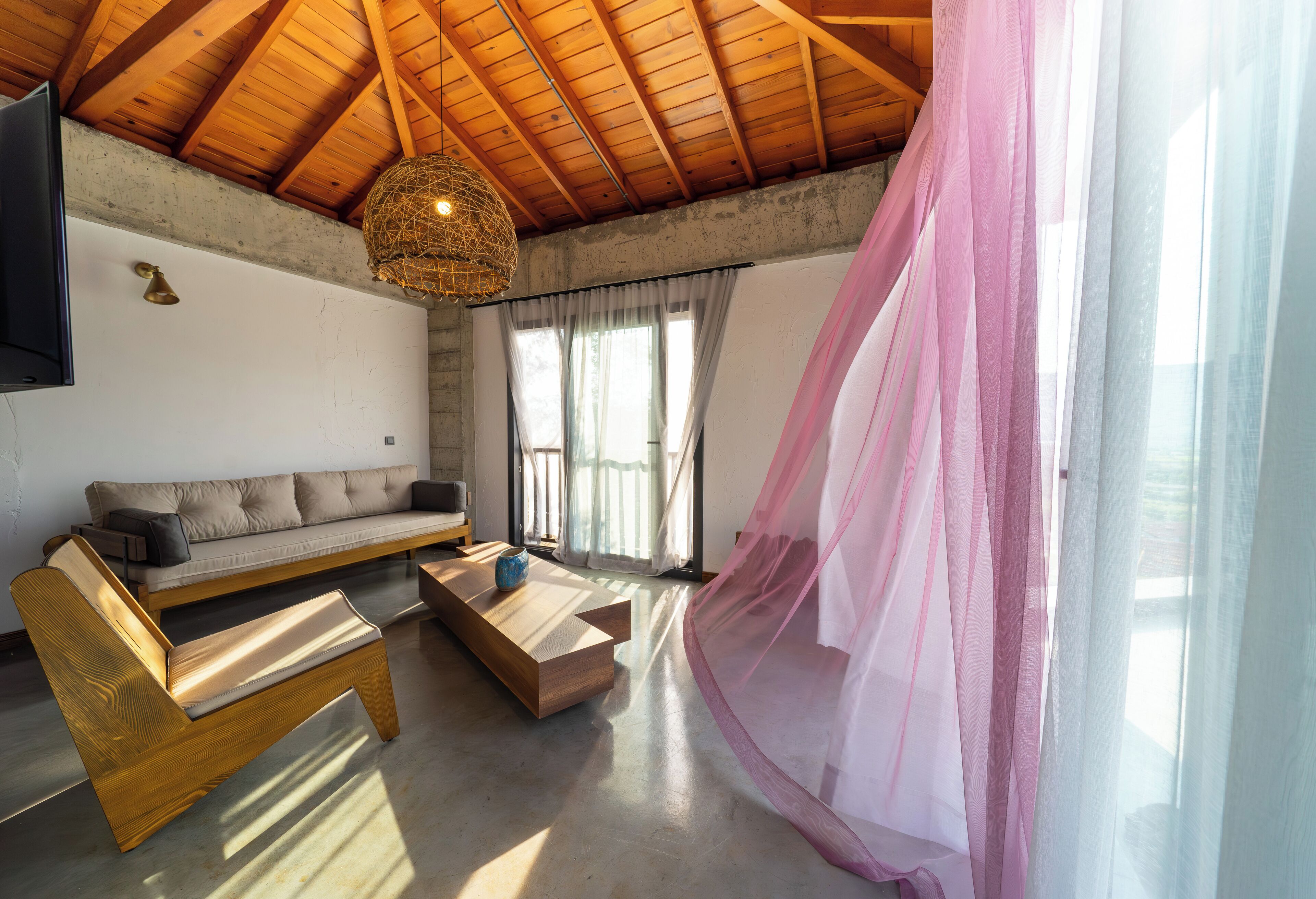 Una sala de estar moderna con techo de madera, un sofá, una mesa de centro y un dosel rosa.