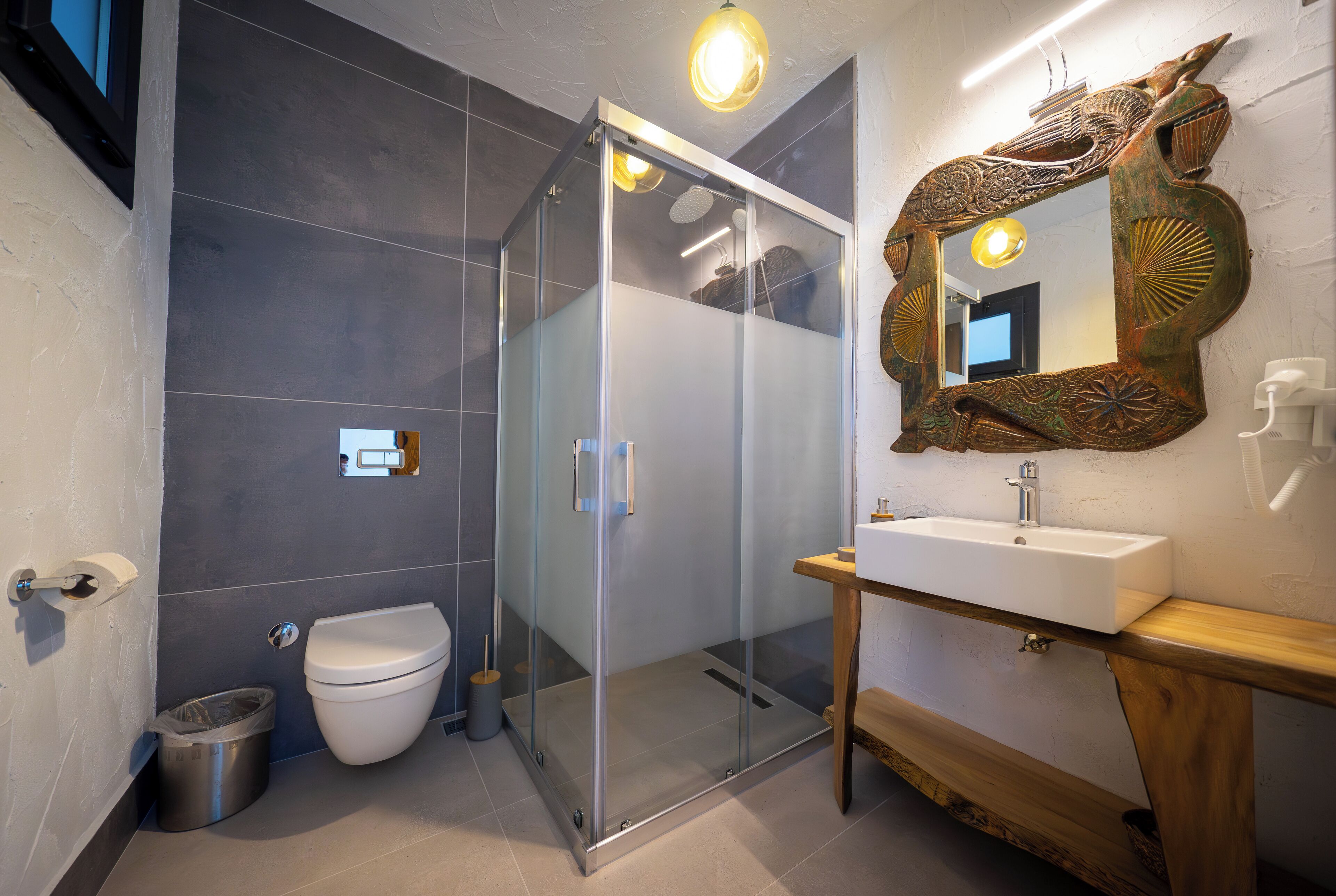 Un bany modern amb plat de dutxa de vidre, un lavabo blanc i un mirall decoratiu.