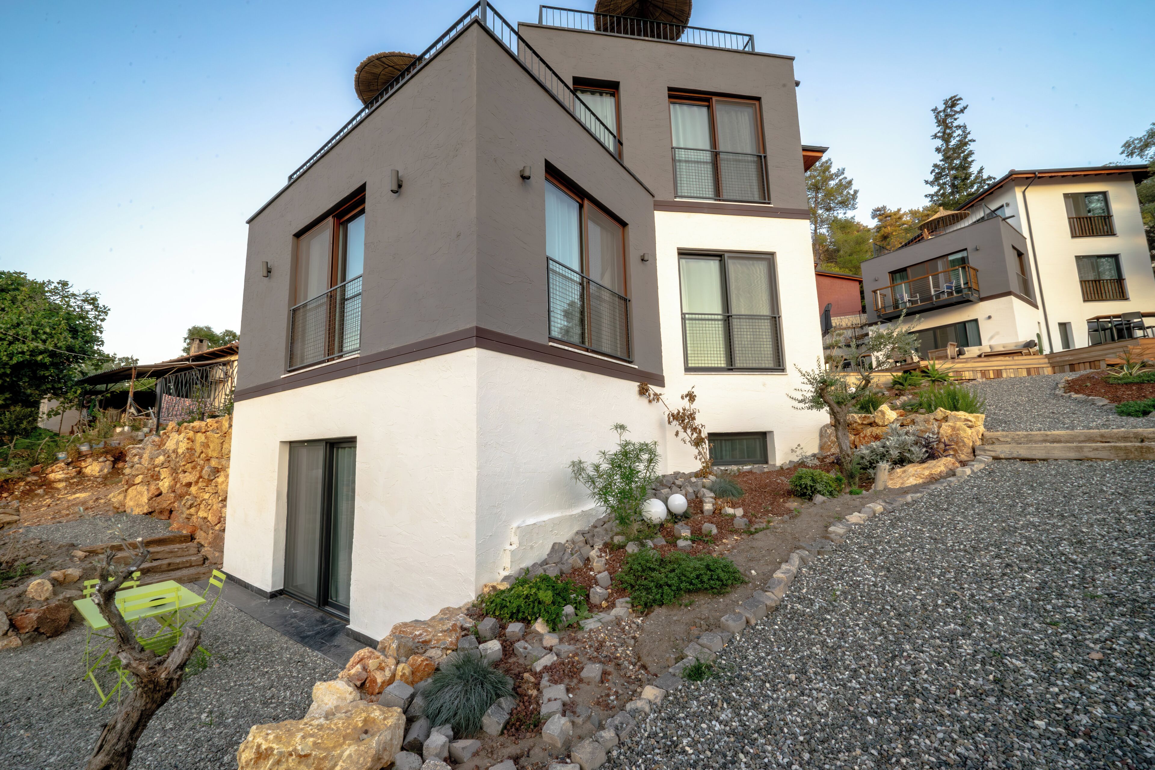 A modern two-story house with a stone facade, a balcony, and a gravel driveway.