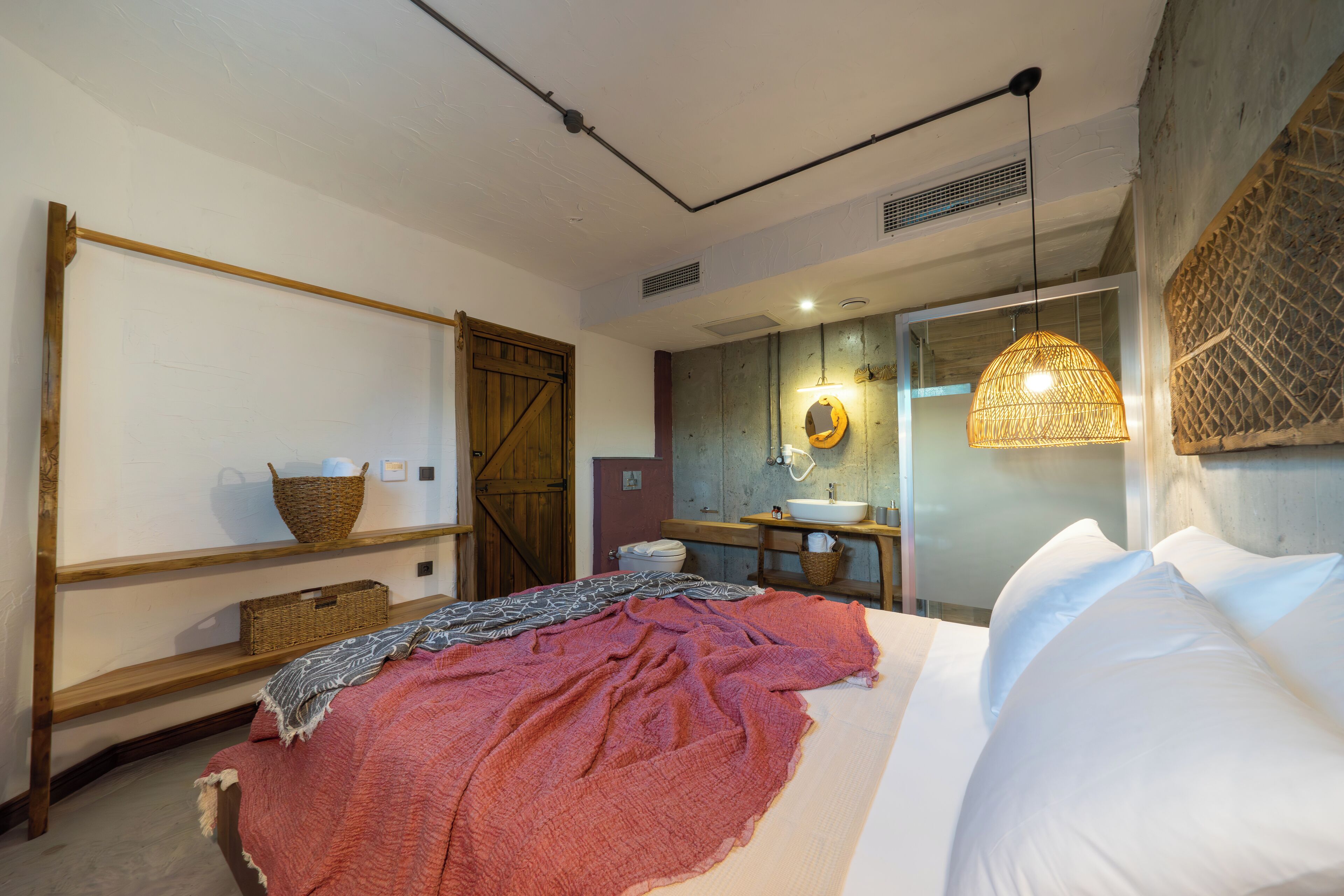 Un dormitorio con una cama, estanterías de madera, una cesta y un baño con lavabo y espejo.