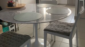 Een moderne keuken met witte kasten, een roestvrijstalen koelkast en een vaatwasser. Er is een eethoek met een glazen tafel en twee stoelen.
