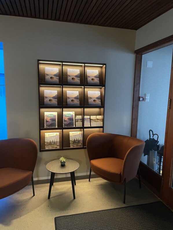 A room with a wall-mounted display of framed pictures, two brown armchairs, a small round table with a plant, and a door with a metal gate.