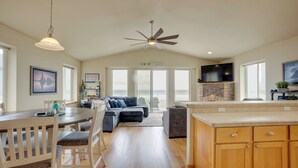 A spacious living area with a dining table, two sofas, a ceiling fan, and a fireplace. - Gold Beach Retreat: Private Hot Tub + Ocean Views! (Gold Beach)